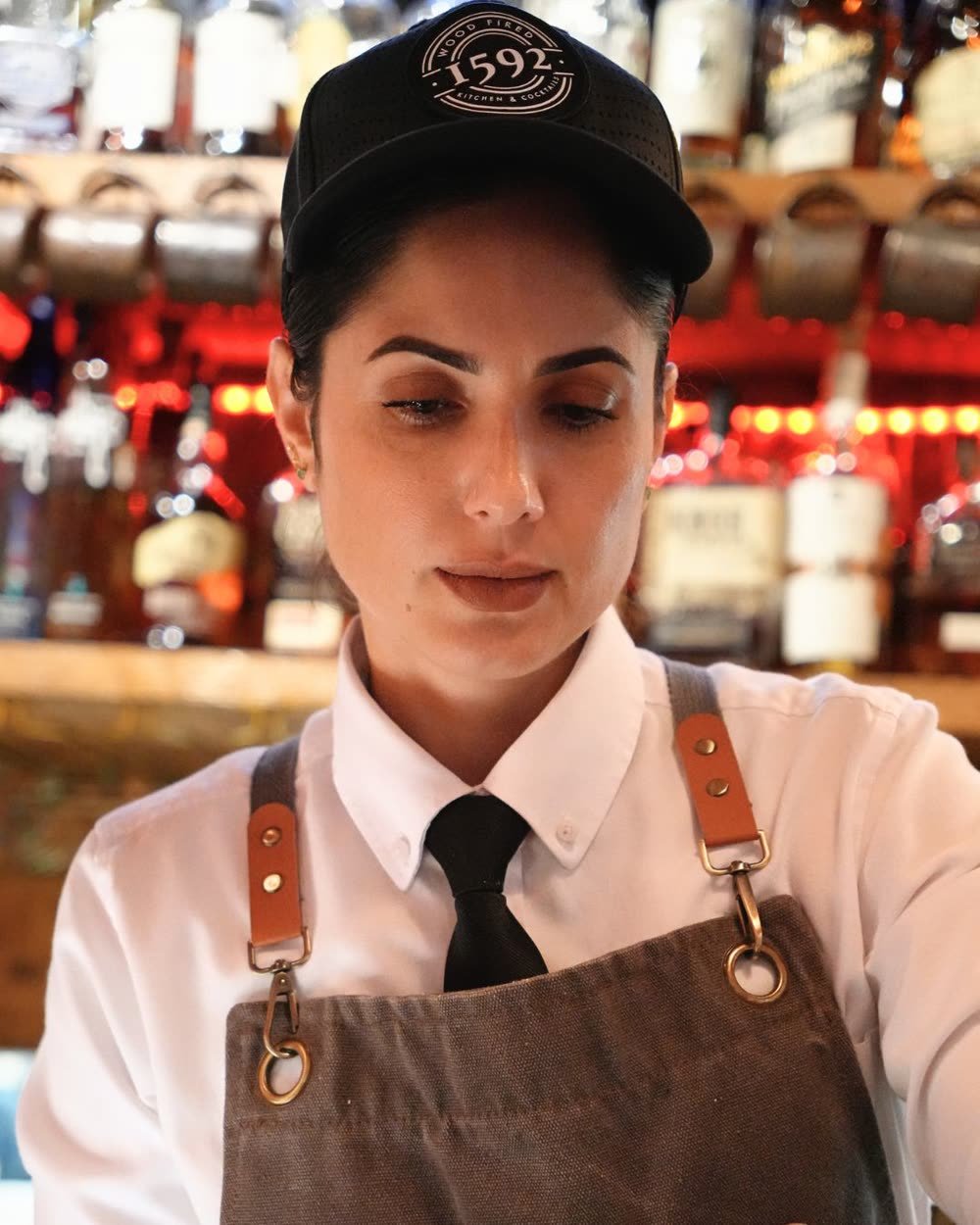 A 1592 Wood Fired server in a 1592 cap, tie and apron behind the bar, Sarasota