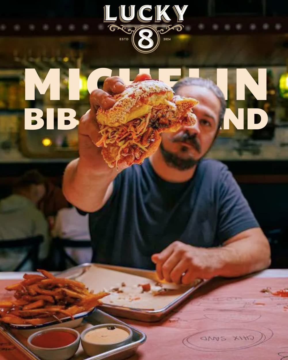 Chef Mark of Lucky 8 SRQ holding a sandwich under the Michelin Bib Gourmand headline, Sarasota