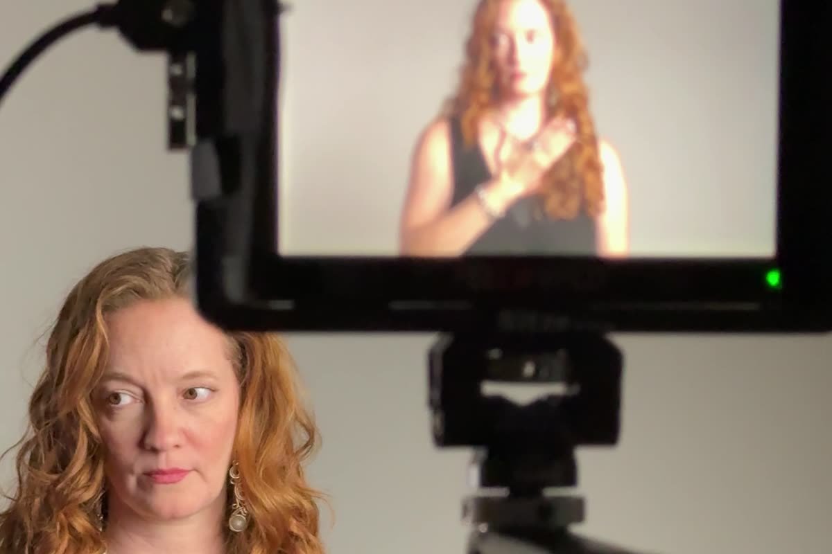 A woman on camera beside the field monitor showing her, during a Siesta Media video shoot